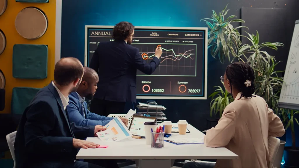 A business team in a meeting, analyzing data trends and discussing strategies on a large screen with graphs and data visuals.